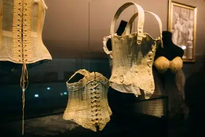 Museum display case with vintage clothing and accessories lit by gallery lighting, with visitors viewing from behind