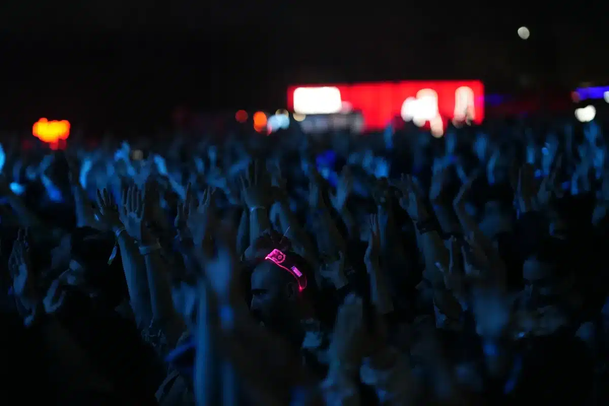 Multitud de fanáticos en un estadio nocturno con las manos levantadas y luces de teléfono brillando en la oscuridad.