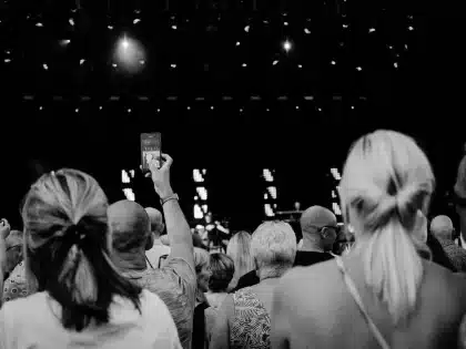 Crowd of concertgoers with raised hands and phone lights during a live performance at an arena venue