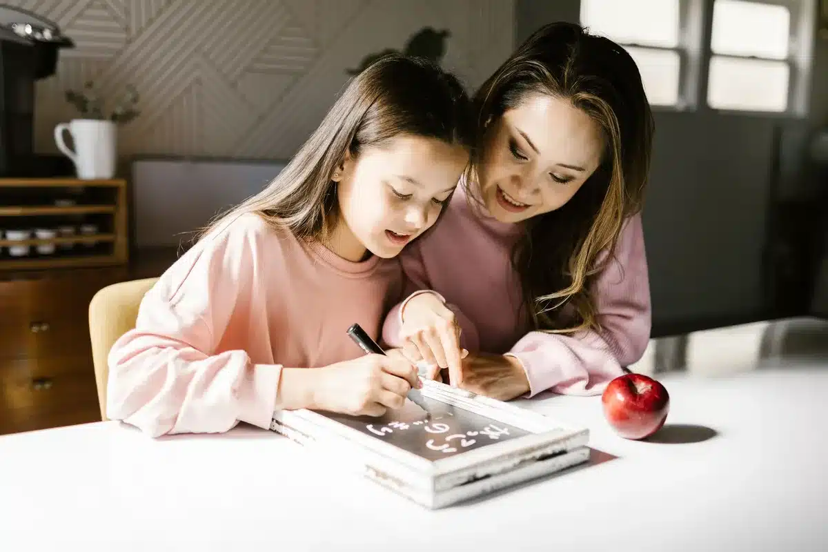 A mother and daughter working together on a writing project, collaborating at a table with papers and notes.