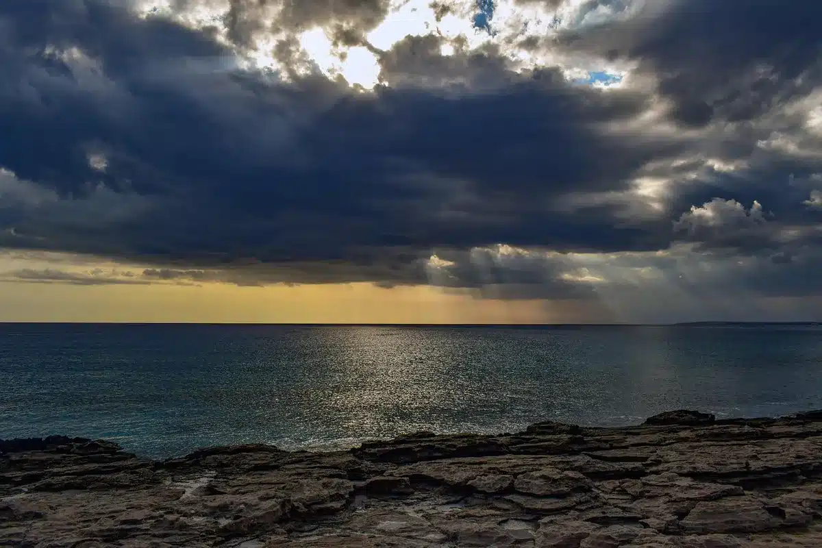 Silhouette of a ship near a rocky coast under rough seas