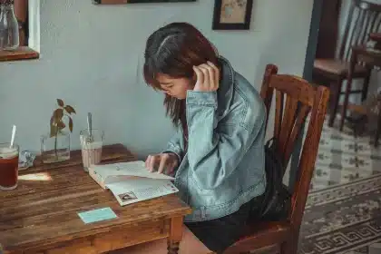 Hands holding a paperback translation of Greek myths with a quiz sheet on a café table